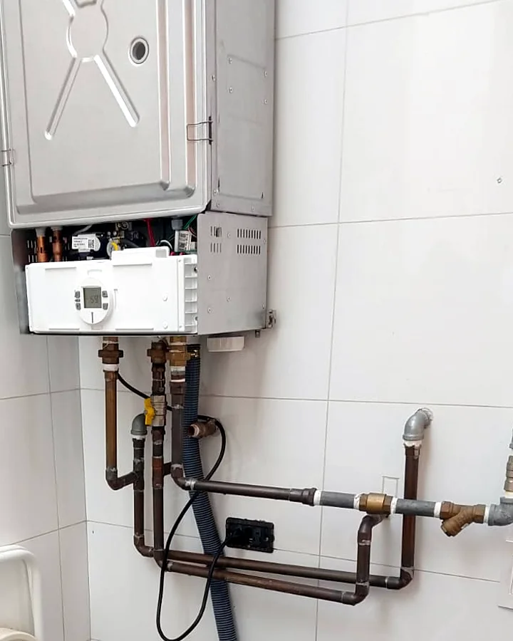 Caldera a gas abierta durante una revisión técnica, con sus conexiones de agua y gas